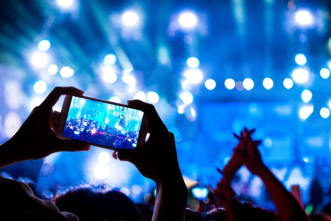 Man taking a video of the show at the concert hall using a smartphone